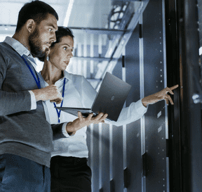 Muž a žena u serverů se dívají do notebooku