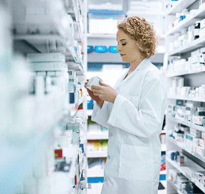 Lékárnice se dívá na krabičku léků v regálech s léky